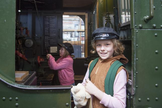 Two girls wearing engine driver caps in the cab of a steam engine