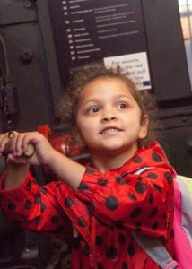 A girl in a red and black polka dot coat pulling a wooden handle