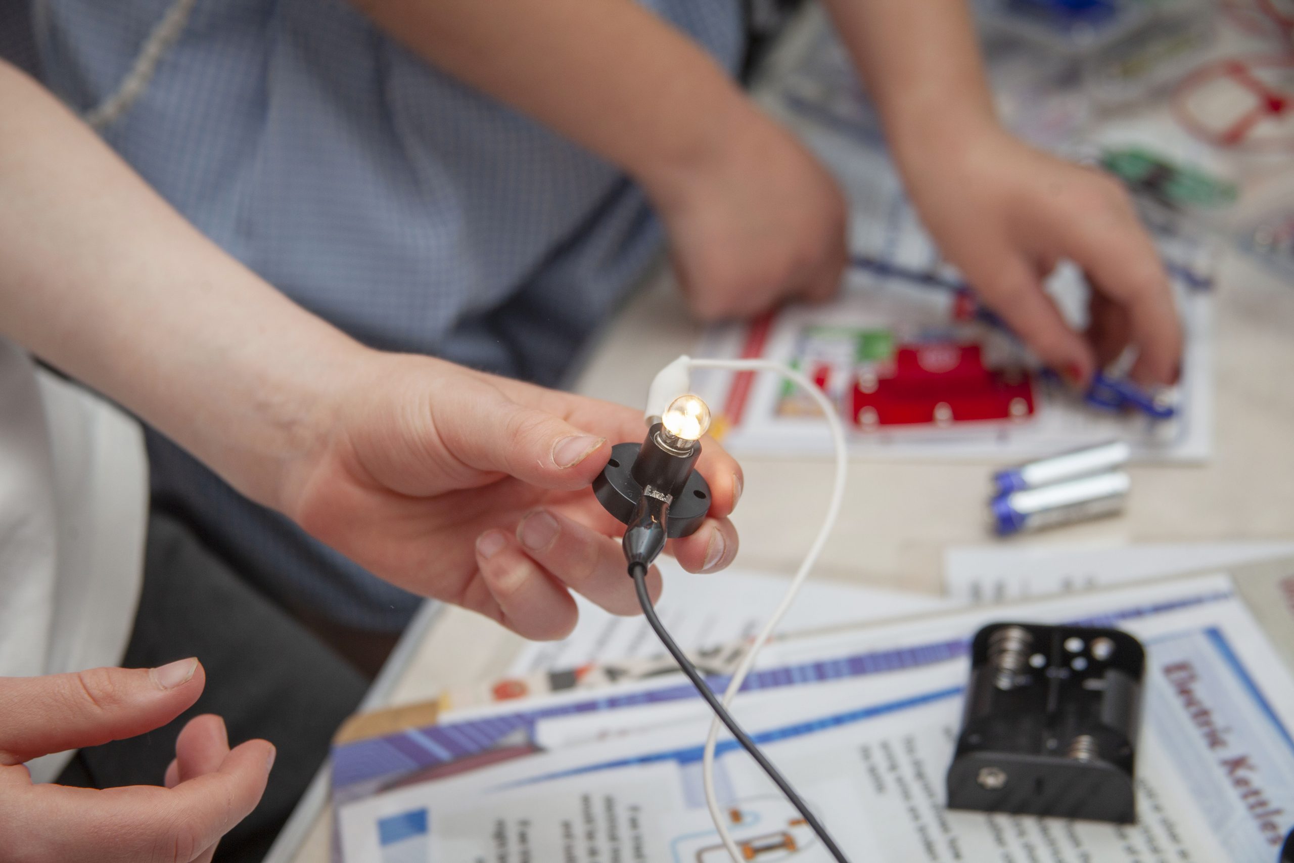 A child's hand holding a lit lightbulb connected to a circuit board. 