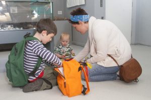 A family sitting on the floor of a museum gallery, looking into a backpack