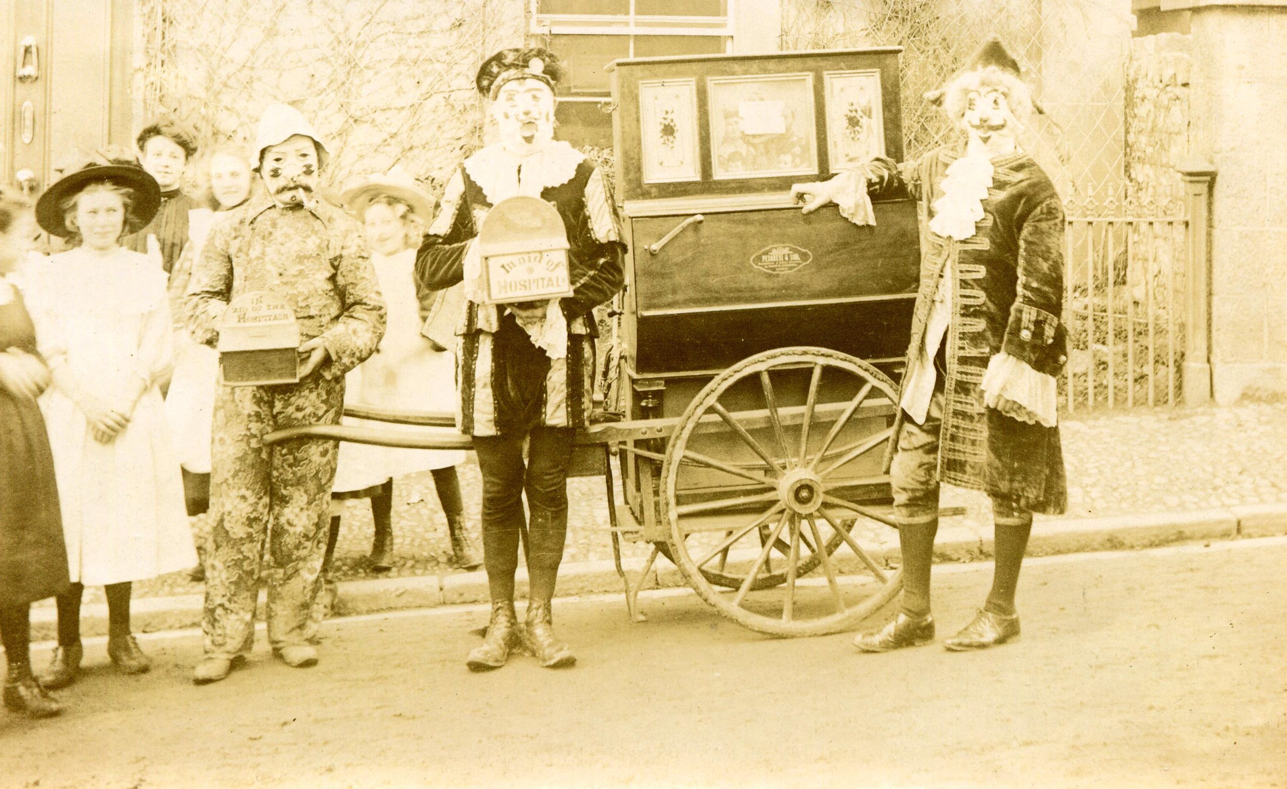 some people in costume stanging round a barrel piano, an organ on wheels, in black and white