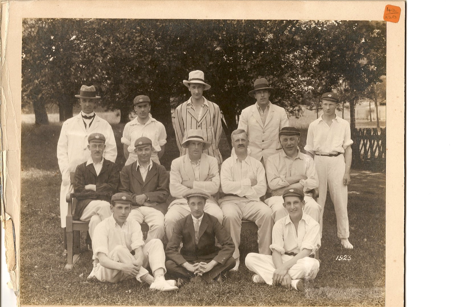 13 men seated in rows wearing old fashioned cricket kit and hats