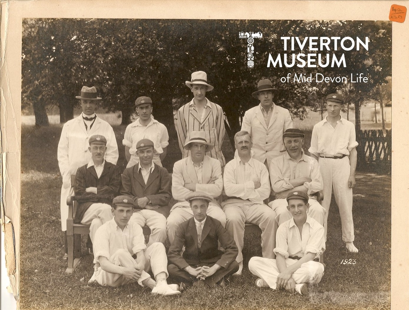 13 men seated in rows wearing old fashioned cricket kit and hats