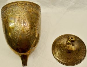 A heavily engraved gold coloured goblet with its base next to it