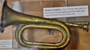 A brass bugle, a brass tube coil with a large horn opening at one end and a mouthpiece at the other.