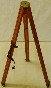 A wooden tripod with a metal disc at the top and a fabric strap around one of the three legs
