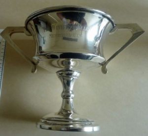 A silver sports trophy cup with a large bowl and two handles engraved 'The Winifred Ellis Memorial Cup' on the bowl.