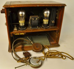 An old radio set in a wooden box open to show the inner working with lightbulbs and wires.