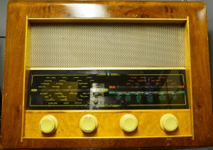 An old radio, a brown wooden rectangular box with a mesh below above some dials and a display showing numbers and frequencies. 