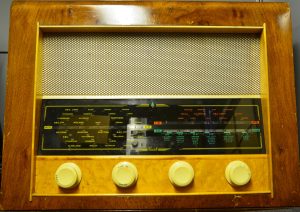 An old radio, a brown wooden rectangular box with a mesh below above some dials and a display showing numbers and frequencies.