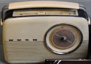 A an old radio - a cream radio, most likely made of Bakelite, with chrome detail and a cream leather effect handle. There is a circular dial on the right and the word BUSH on the left in chrome letters.