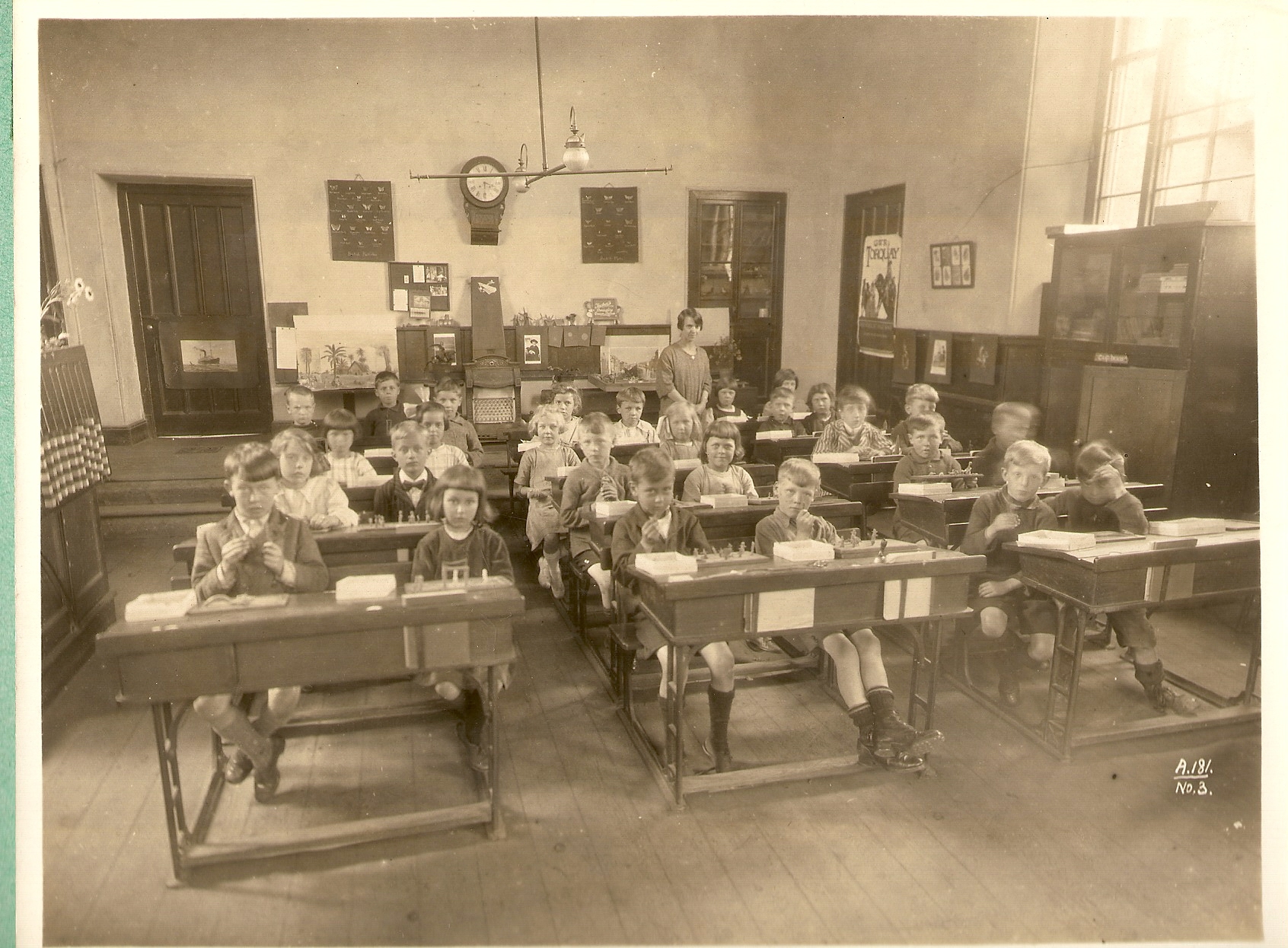 A black and white photo of a school room with children sitting at desks
