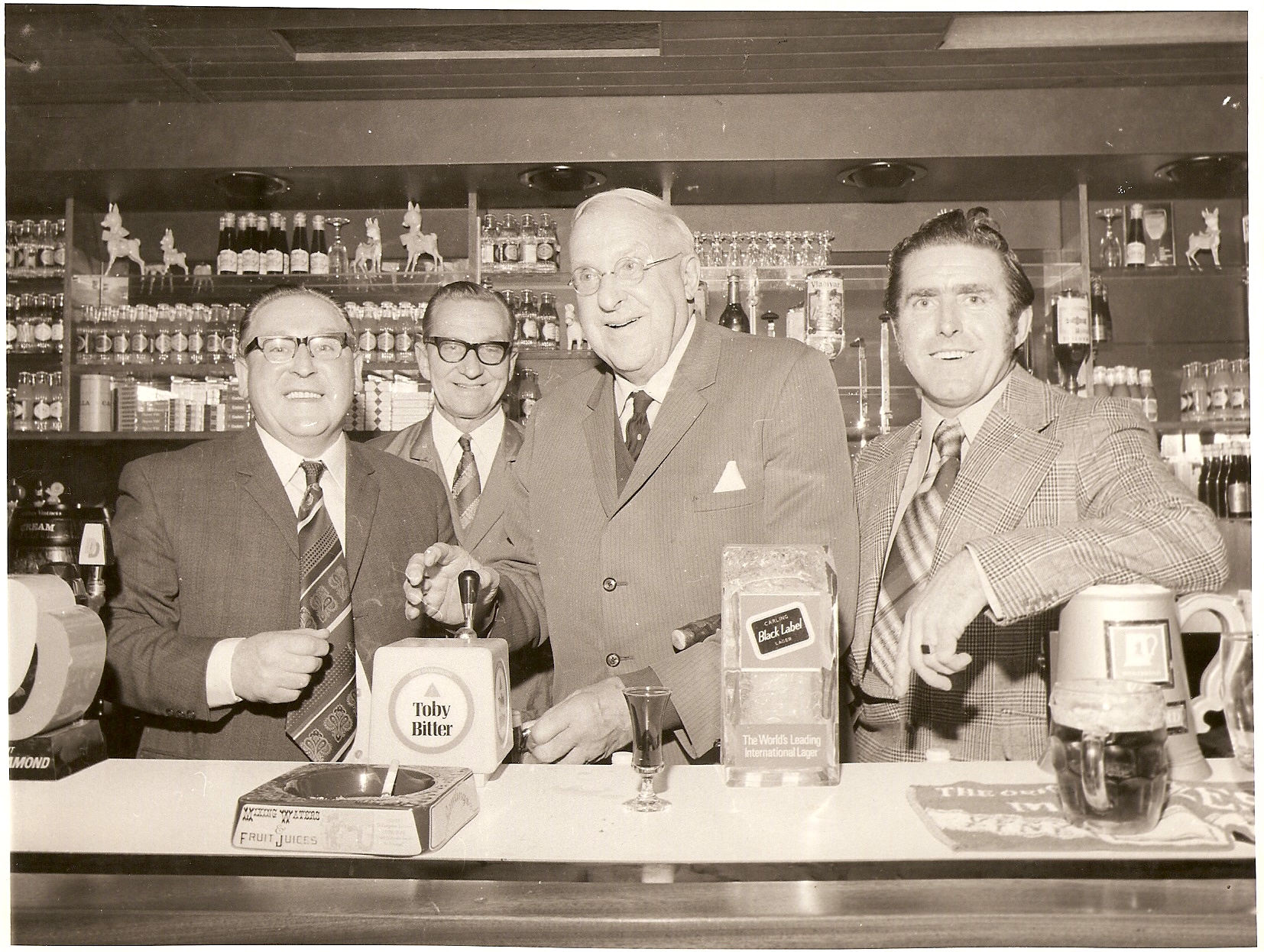 4 men standing behind a bar. One is pulling a pint.