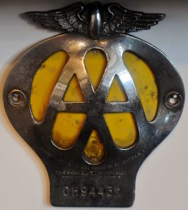 A badge or plaque made of a silver coloured medal. It features a bird shape at the top with two large cut out capital letter As in the middle of the badge with a yellow background behind. At the bottom of the badge there is a membership number.