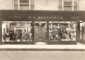 A shop front with double windows. The windows have all sorts of coats and hats on display.