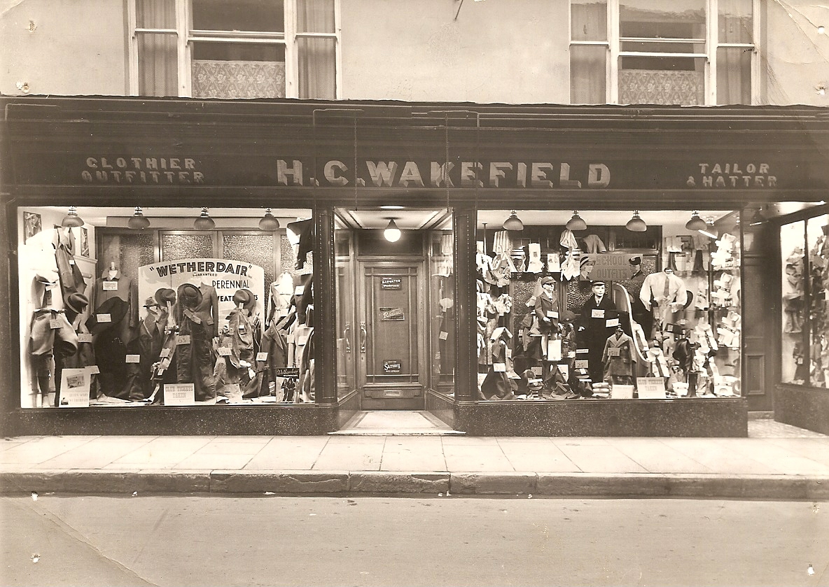 A shop front with double windows. The windows have all sorts of coats and hats on display.