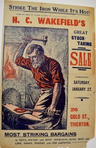 A colour newspaper advert for Wakefield's featuring an illustration of a blacksmith hammering a red hot horseshoe. It reads 'Strike The Iron While It's Hot!'. The advert is promoting a sale.