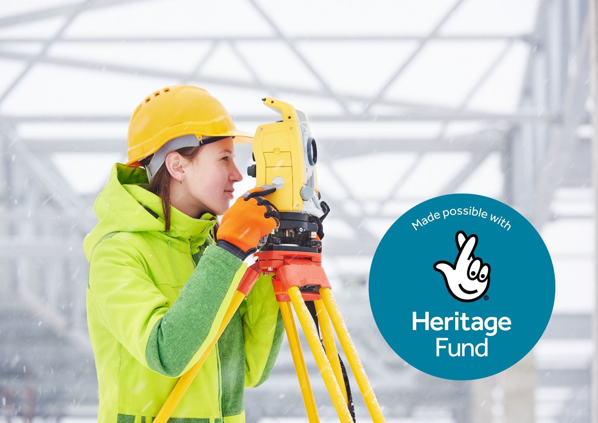 A white woman in a hi-vis jacket and hard hat looking through surveying equipment