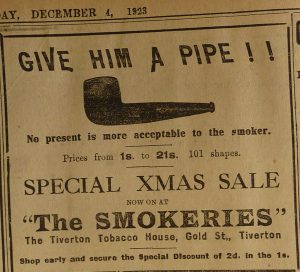 Newspaper Advert for 'The Smokeries' Tiverton Tobacco House. The slogan is 'Give Him a Pipe!' and there is an illustration of a smoking pipe with the tagline 'no present is more acceptable to the smoker'. 