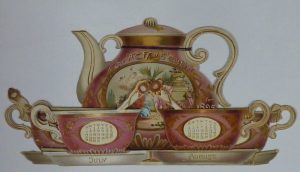 A calendar in the shape of a teapot with two teacups. Both teapot and cups are pink with white and gold trim. The teapot features the wording 'The At Home Calendar for 1895'. One of the teacups says 'July, the other 'August' and both feature the dates of those months respectively. 