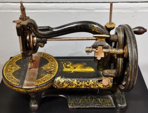 Small black hand crank sewing machine with ornate looking gold designs