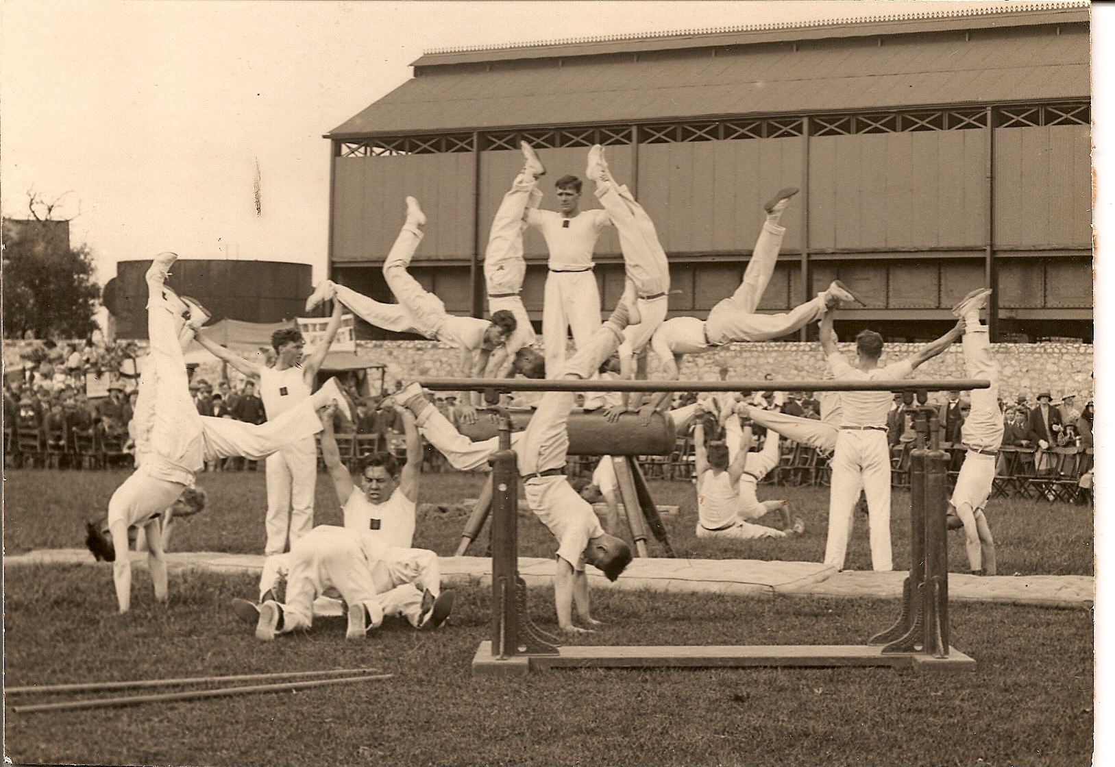 A group of men in white trousers and tops performing what looks like a gymnastics display.