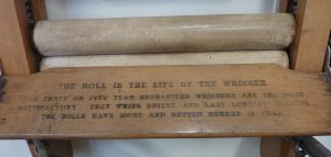 A close up of some wording on a mangle that reads 'The roll is the life of the wringer. Three or five year guaranteed wringers are the most satisfactory. They wring driest and last longest because the rolls have more and better rubber in them. 