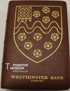 A brown money box in the style and shape of a leather bound book. 