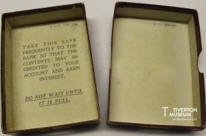 The inside of a money box which reads 'Take this safe regularly to the bank so that the contents may be credited to your account and earn interest. Don not wait until it is full.' 
