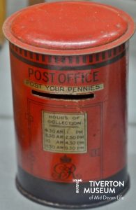A red tin money box in the shape of a postbox. 