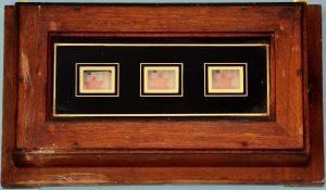 Wooden case with glass front. Contains electrical mechanism for three moving plates which show where in house electric bell to summon servent has been pressed