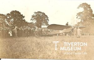 A crowd is gathered in a field looking at an early plane.