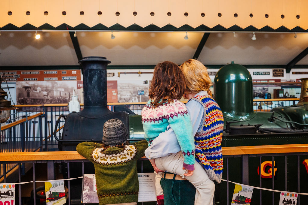 Two girls wearing engine driver caps in the cab of a steam engine